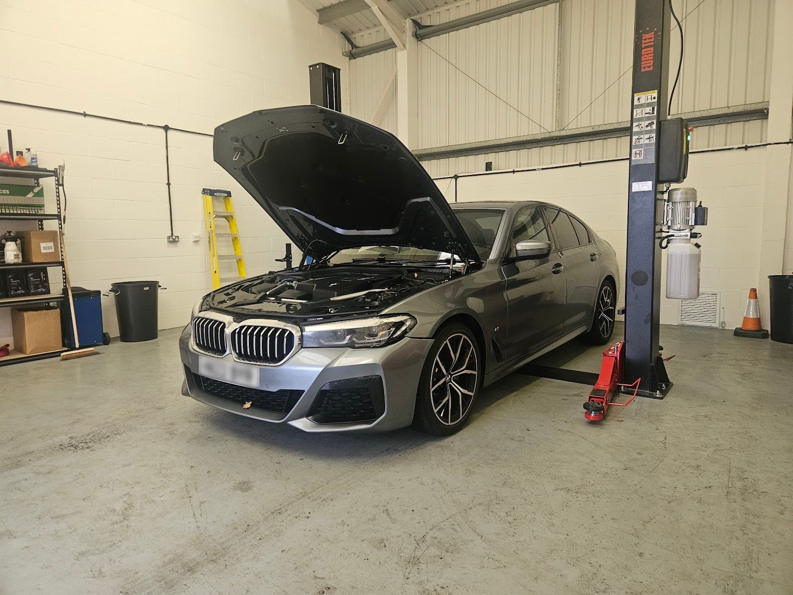 Grey BMW with its bonnet open on a lift during servicing at Brookswood Automotive